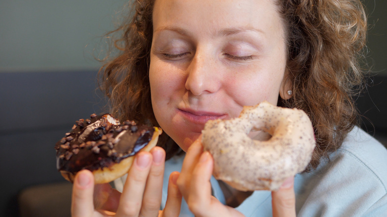 Binge eating concept. Attractive Caucasian woman with eating disorder eating two donuts quickly and at the same time
